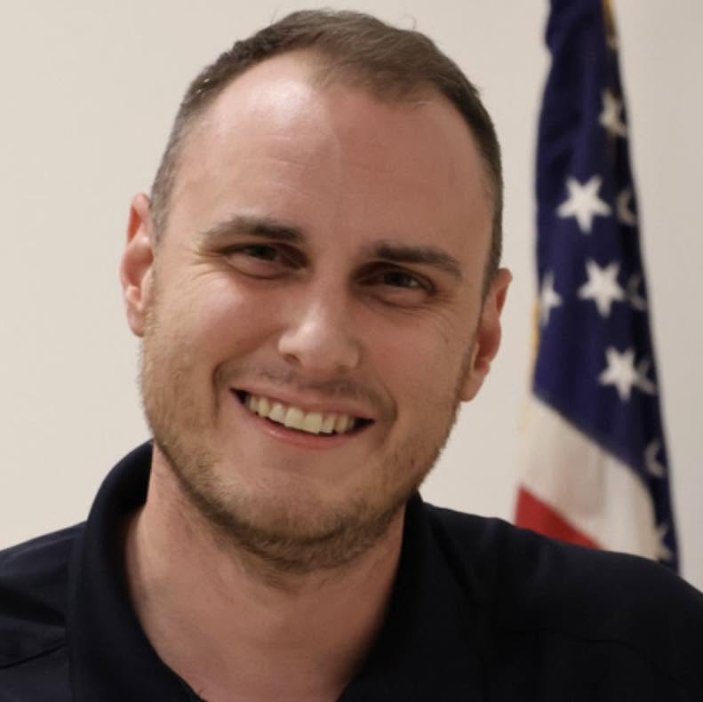 David Patty, smiling, with an American flag behind him